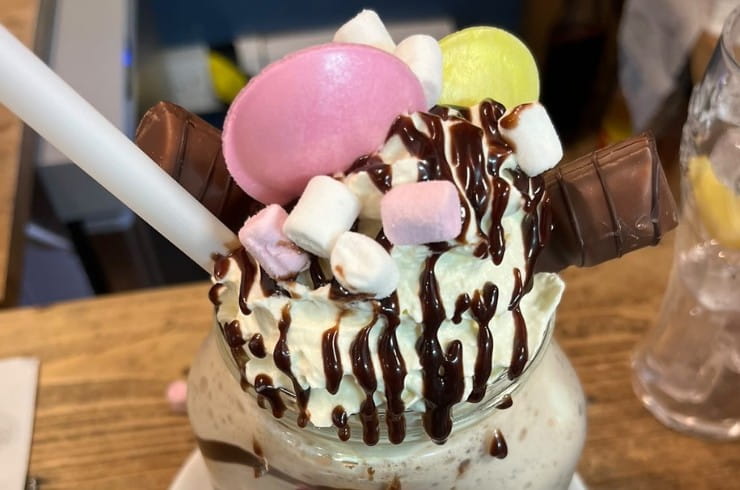 A milkshake topped with whipped cream, mini marshmellows and chocolate sauce