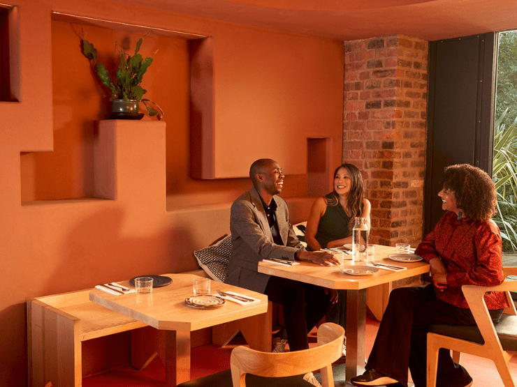 Three people having dinner in a restaurant with orange walls