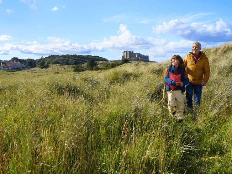 A family with a child holding a kite and Bamburgh Castle visible in the background